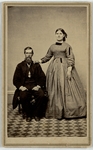 Older bearded man wearing a tuxedo and long coat sitting down with young girl with hair parted down middle tied with ribbon wearing long dress standing to his left, front by J. R. Brown