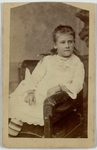 Girl in white dress sitting with arm draped casually over armrest, front