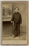 Boy in jacket with hard combed to the side standing with arm rested on small table with a painting of a church in background, front by Joshua A. Williams