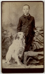 Boy in dark suit standing next to dog, front