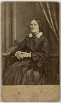 Woman in silk dress sitting with arm on table, facing left, front