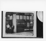 [Donna] Photograph of Two Individuals Posing In Front of Henney Buggy Dealer/Donna Grain Ice Implement Store by Studer, S.A. Tex.